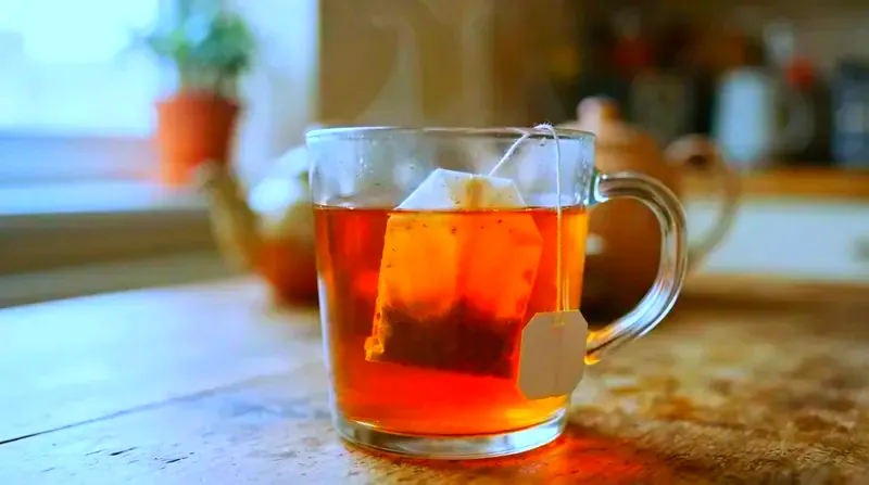 Close-up of a paper tea bag steeping in amber water in a glass mug